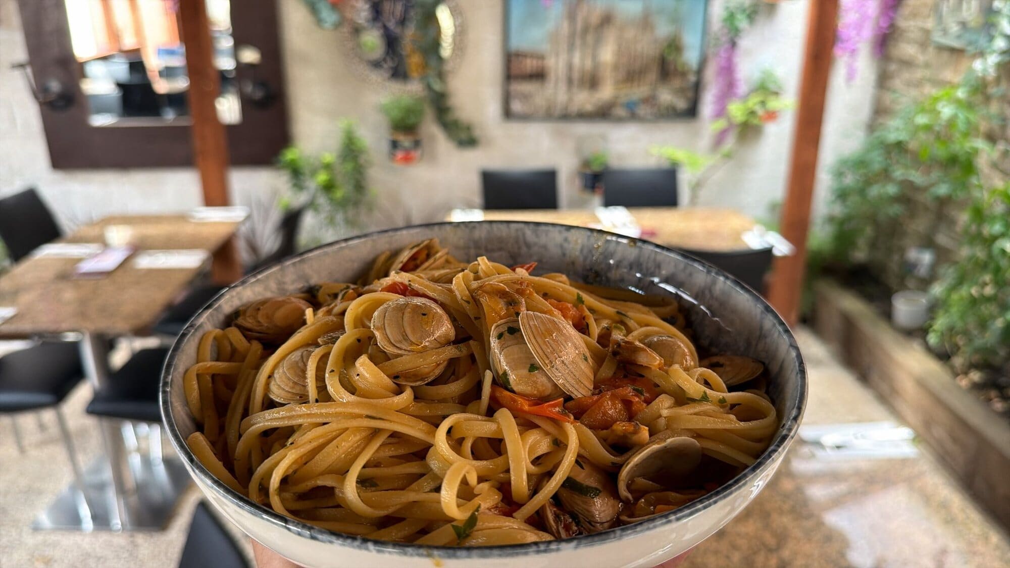 A bowl of linguine vongole with clams and cherry tomatoes, held up in Fabio's covered outside dining area