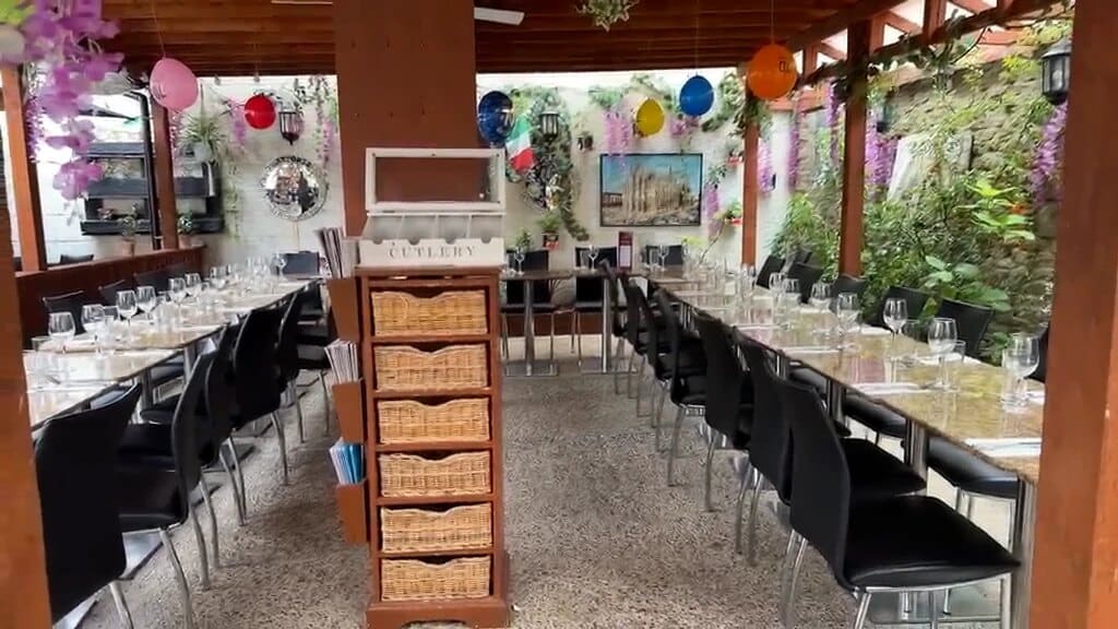 Fabio's covered outside dining area with long tables laid for a party, wicker cutlery stand, balloons and hanging flowers