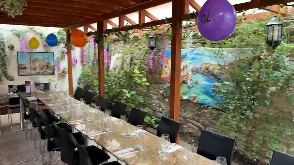 Long table laid under the wooden pergola in Fabio's outside dining area, beside a painted Italian harbour mural and climbing plants