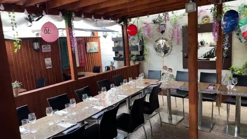 Tables laid for a celebration in Fabio's outside dining area, with wooden panelling, green and red shutters and party balloons