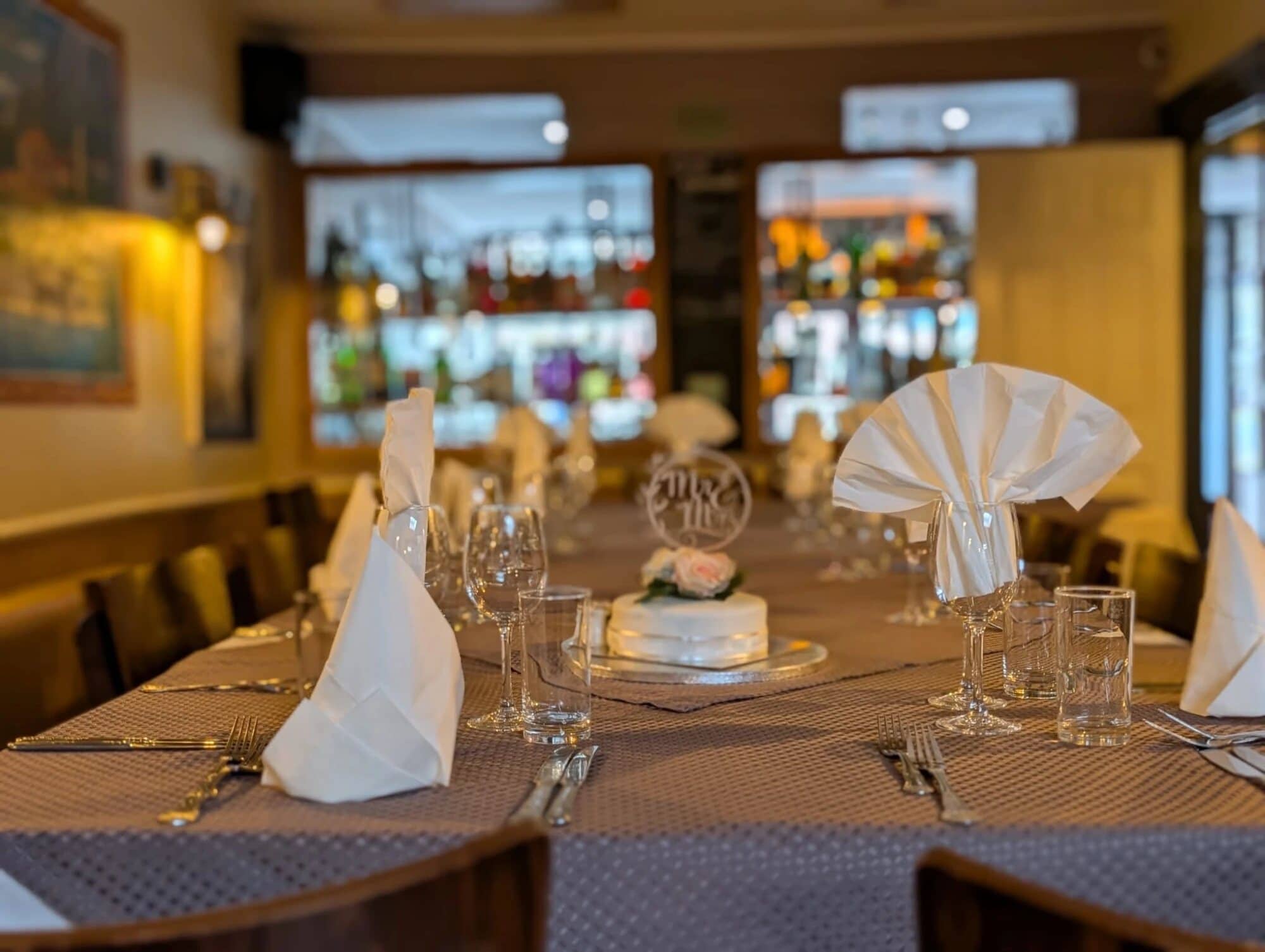 A long table dressed for a wedding party at Fabio's, with folded napkins, glasses and a small white wedding cake with a Mr & Mrs topper